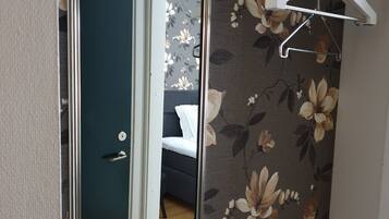 Een kamer met een spiegel die een bed en een deur weerspiegelt, bloemenbehang en een witte kleerhanger aan de muur.