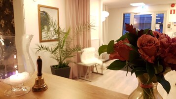 Una habitación con una mesa de madera, un florero de rosas, una vela y una planta en maceta.