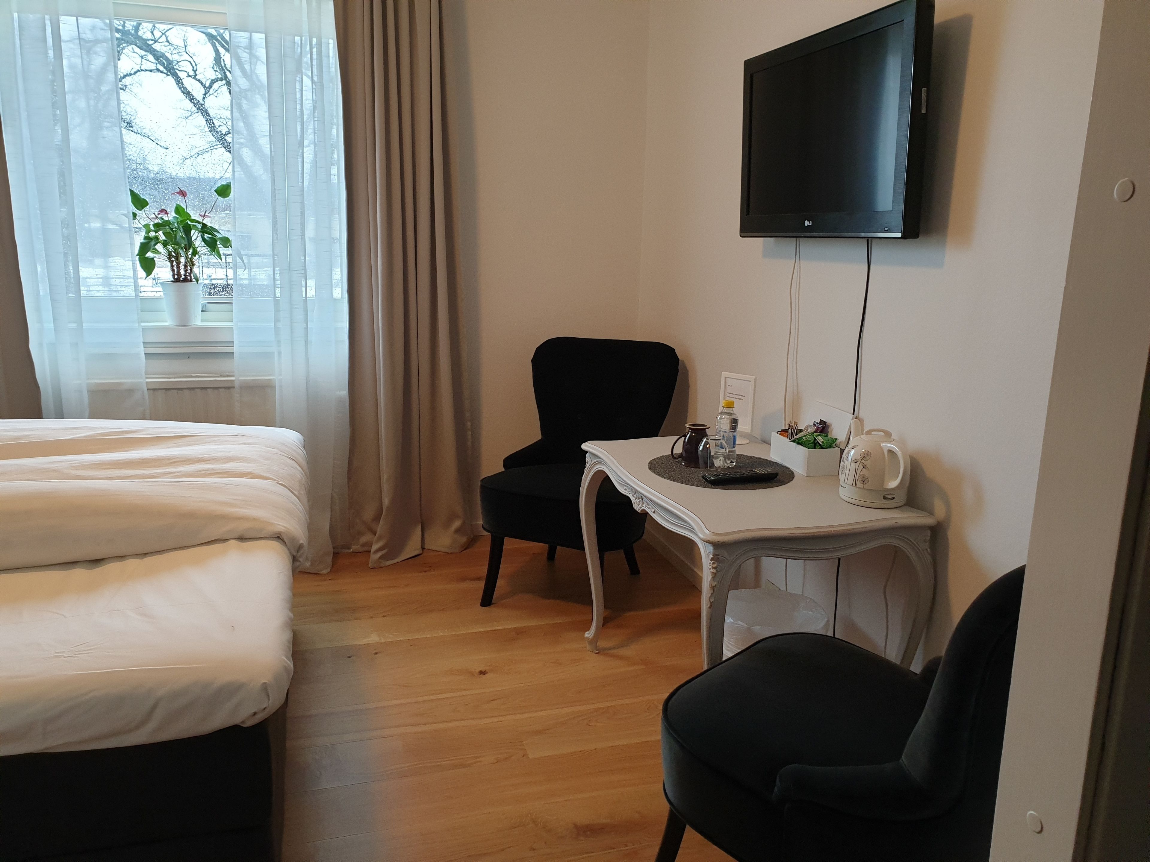A hotel room with a bed, a desk with a chair, a TV, and a window with curtains.