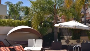Un área de piscina con sillones reclinables, una zona de estar techada y una piscina con escalera.