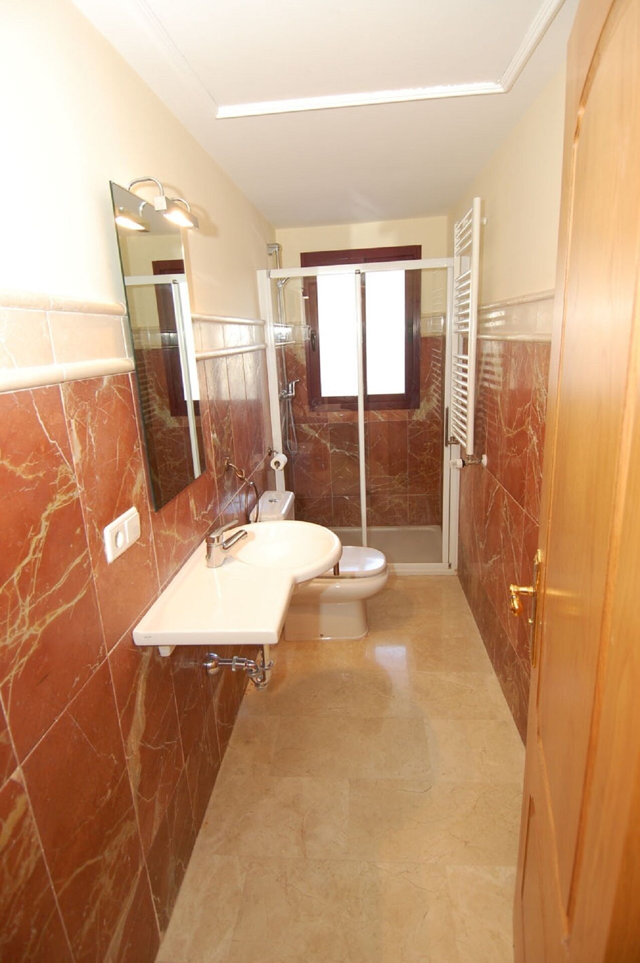 Ein Badezimmer mit Marmorplatten, einem Waschbecken, einer Toilette und einer Duschkabine.