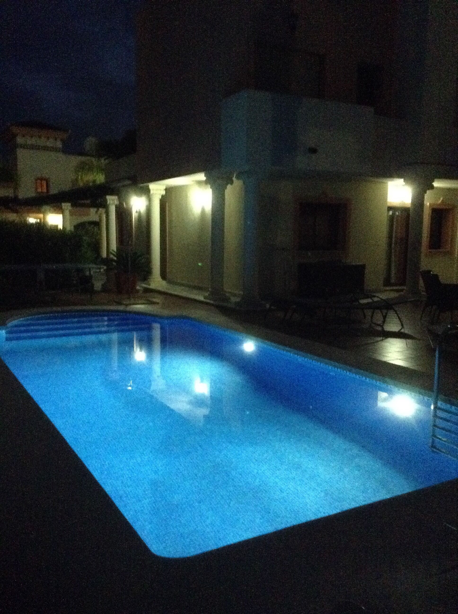 A swimming pool at night with surrounding buildings and outdoor seating.