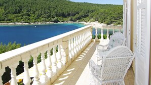 A balcony with white wicker furniture, a view of a turquoise sea, and a forested hillside. - Luxury house with pool, direct beach & jetty access, stunning 270° sea view  (Vela Luka)