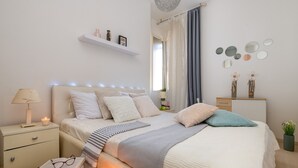A neatly arranged bedroom with a bed, bedside tables, a nightstand, and a shelf with decorative items.