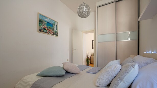 Una camera da letto con un letto, cuscini, un quadro e una lampada a sospensione.