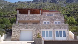A two-story stone building with a garage, a balcony, and a staircase leading to the upper floor. - Magnificent Newly-built Villa in Mlini with Private Pool and Near Beaches (20207 Mlini)