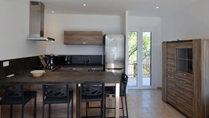 Una cocina moderna con una isla central, electrodomésticos de acero inoxidable y un amplio ventanal corredera que da a un espacio exterior.