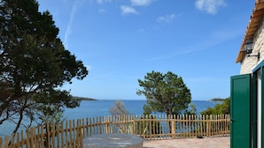 Un patio de piedra con un cerco de madera, una mesa de piedra y vista al mar.