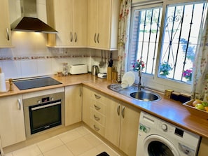 A kitchen with a Bosch oven, a washing machine, and a window with floral curtains.