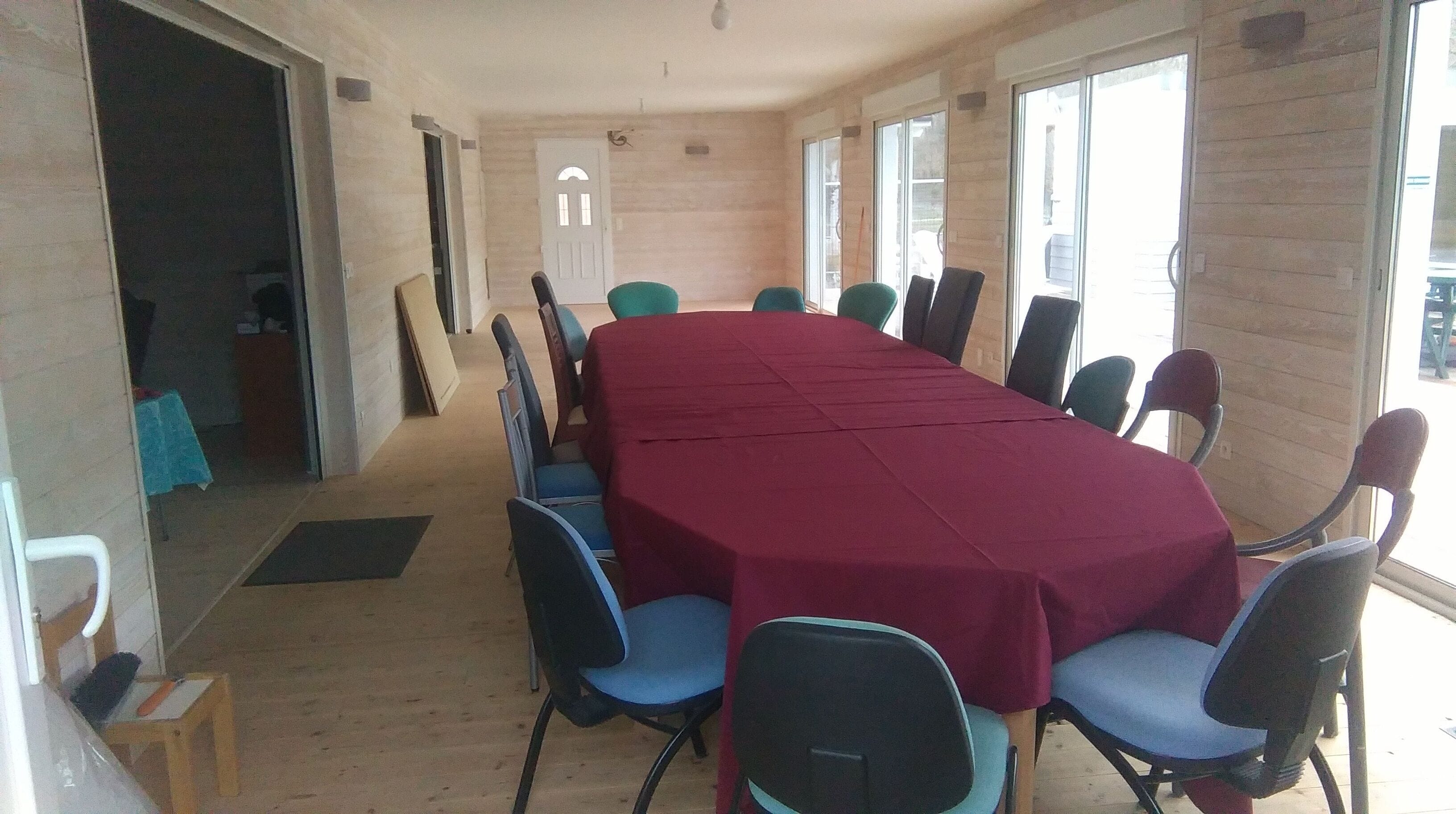 Une salle de conférence avec une longue table recouverte d’une nappe rouge, entourée de chaises bleues.