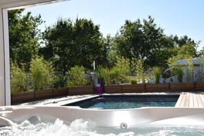 A hot tub with a wooden deck and a pool in the background, surrounded by lush greenery. - Beautiful 300 m² house with heated swimming pool and spa Close to the ocean (Grayan-Et-L'hôpital)