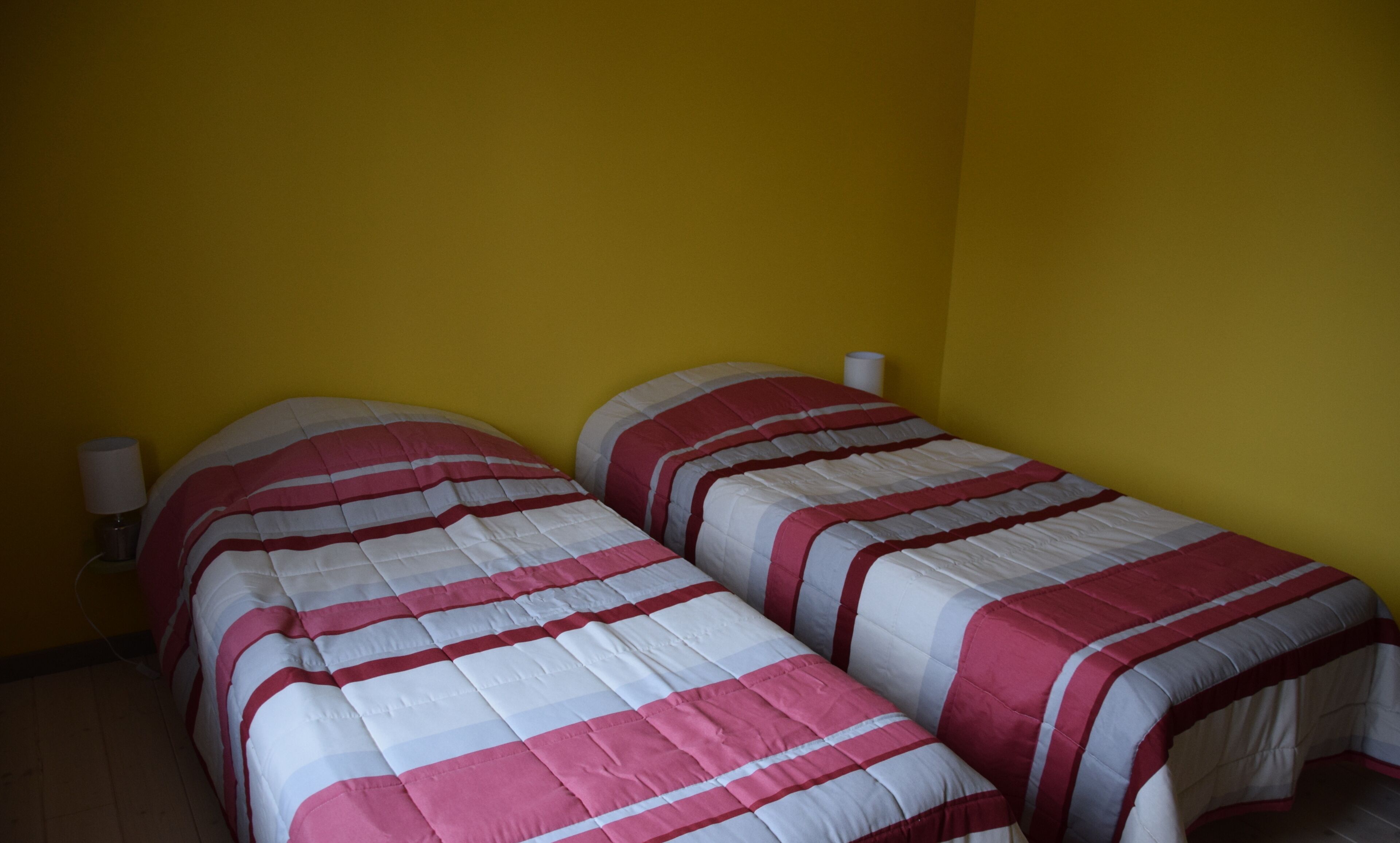 Two single beds with striped bedding in a room with yellow walls.