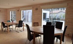 A modern dining area with a wooden table and black chairs, large windows, and a view of the outside.