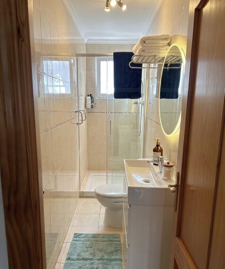 Un ba ño con cabina de ducha de vidrio, inodoro, lavabo con espejo y toallero.