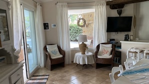 A cozy room with wicker chairs, a small table with a lamp, a TV, and a dining area with chairs and a table set for two.