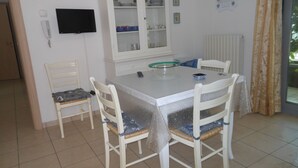 Uma sala de jantar com mesa, cadeiras, um armário e uma televisão na parede.