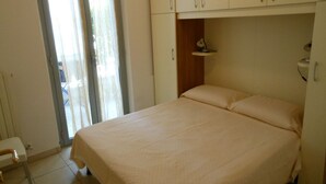 Um quarto com cama, uma cadeira e um guarda-roupa.