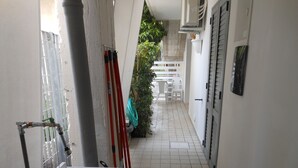 Um corredor estreito com chão de azulejos, um banco branco e uma planta verde.
