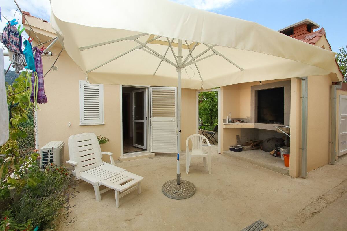 Uma área externa coberta com um guarda-sol branco, uma poltrona branca e uma pequena mesa.