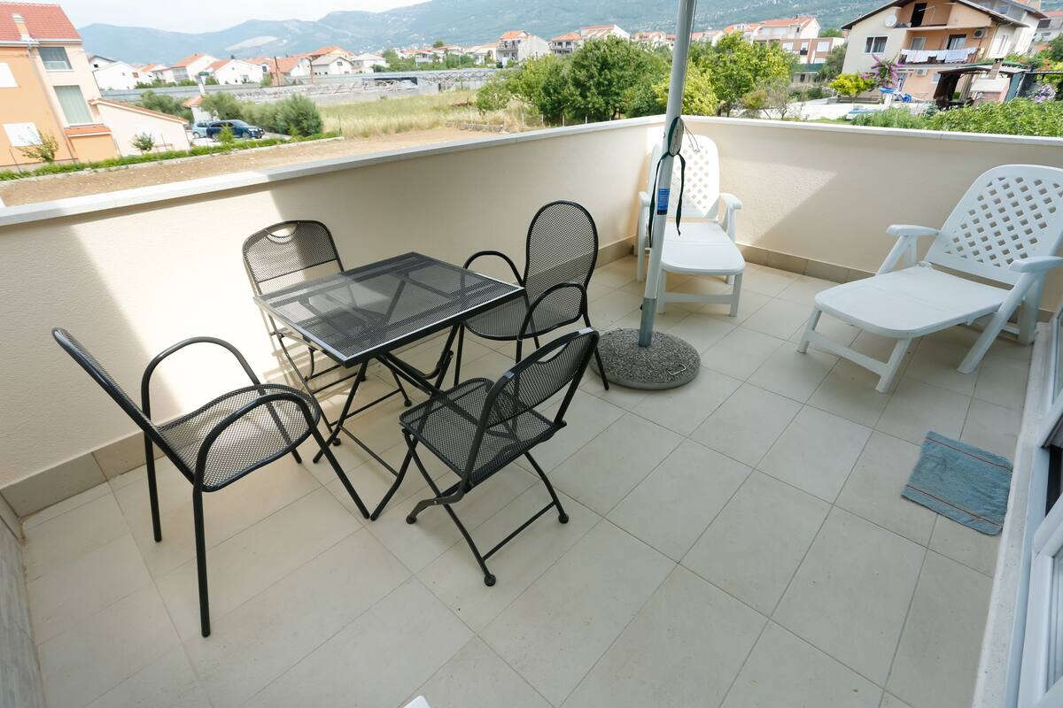 Uma varanda com uma mesa e cadeiras, uma pequena mesa redonda e uma cadeira branca.