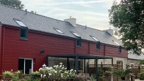 A red building with a sloped roof, a covered patio area, and a garden with various plants and flowers.