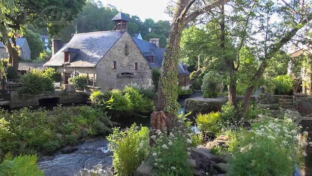 A stone building with a sign that reads "Restaurant" surrounded by lush greenery and a flowing stream.