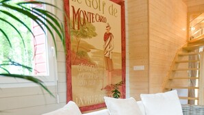 A wicker sofa with white cushions in a room with wooden walls and a poster on the wall.