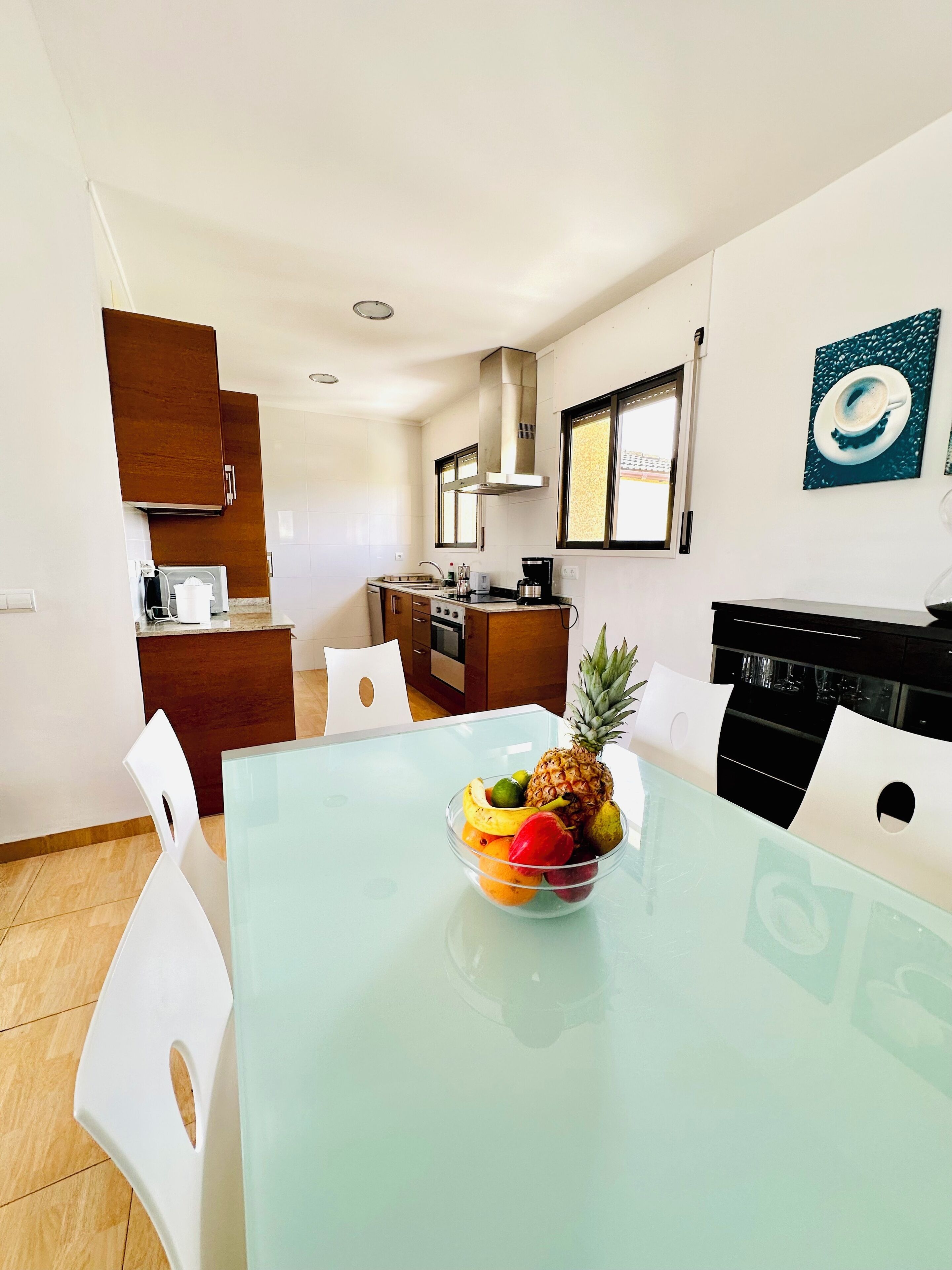 Una cocina moderna con armarios blancos, una mesa de comedor de vidrio y un frutero.