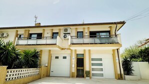 Um edifício de dois andares com telhado plano, aparelhos de ar condicionado e entrada com portão.