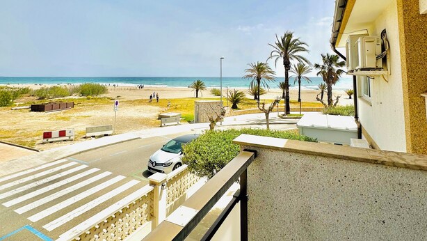 Varanda com vista para uma praia, palmeiras e uma estrada com carros.