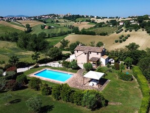 Une grande maison avec une piscine, entourĂ©e dâune vĂ©gĂ©tation luxuriante et de douces collines.