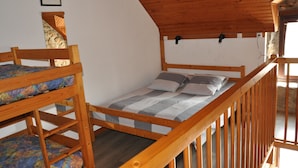 Une chambre de dortoir avec des lits superposés, des poutres en bois et un mur en pierre.