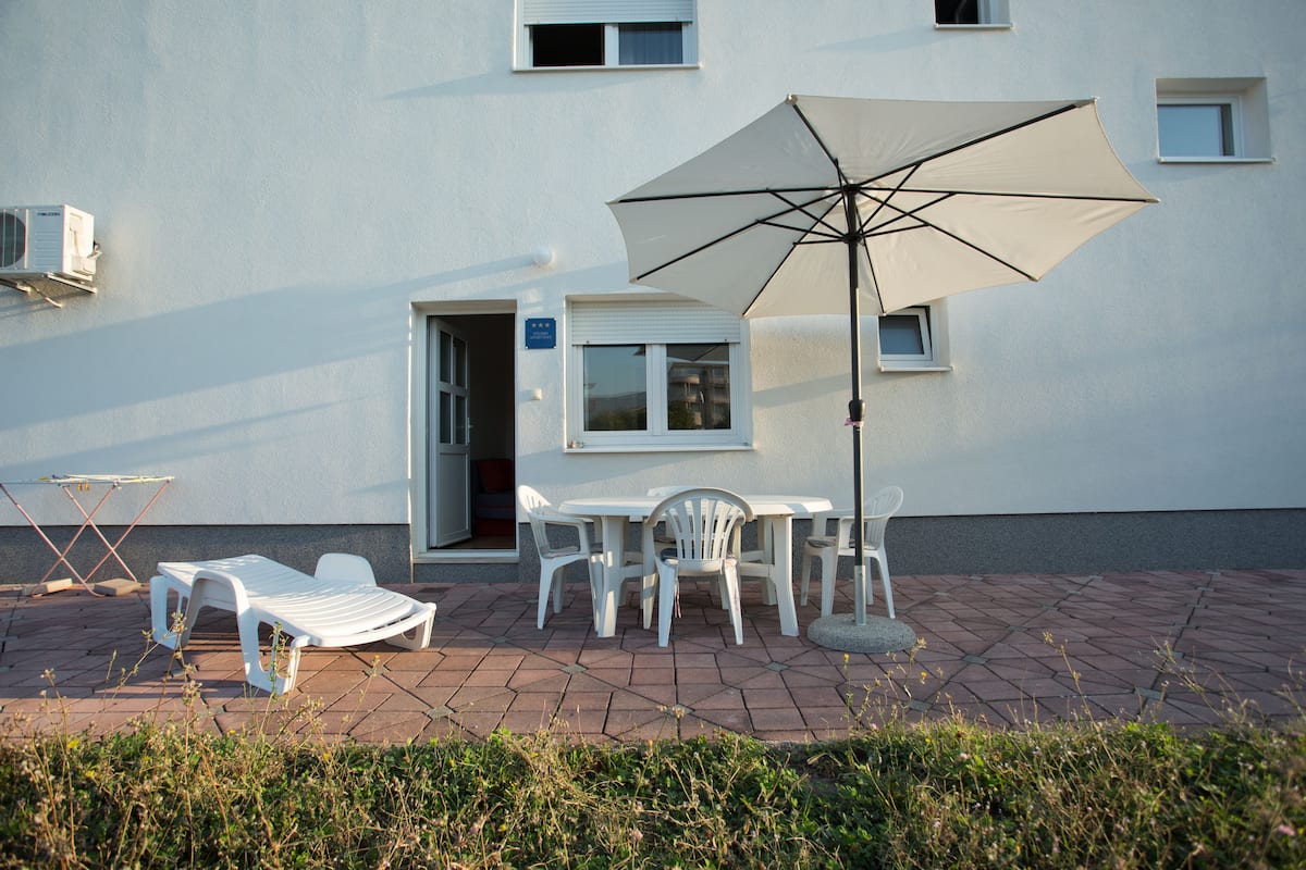 An outdoor seating area with a table and chairs, a sun umbrella, and a white lounge chair.