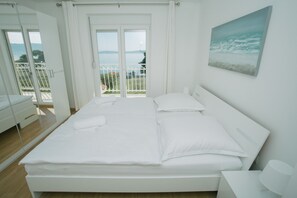 A modern bedroom with a large bed, a balcony with a view of the sea, and a painting on the wall. - Beach Apartments Rumin (Kastela)