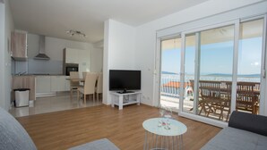 Un salon moderne avec un téléviseur à écran plat, une table basse ronde et un canapé. Il y a un balcon avec vue sur la mer.