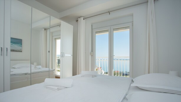 Une chambre d’hôtel avec un grand lit, un miroir et un balcon donnant sur la mer.