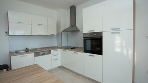 Une cuisine moderne avec des meubles blancs, une hotte en acier inoxydable, un four encastré et un plan de travail en bois.