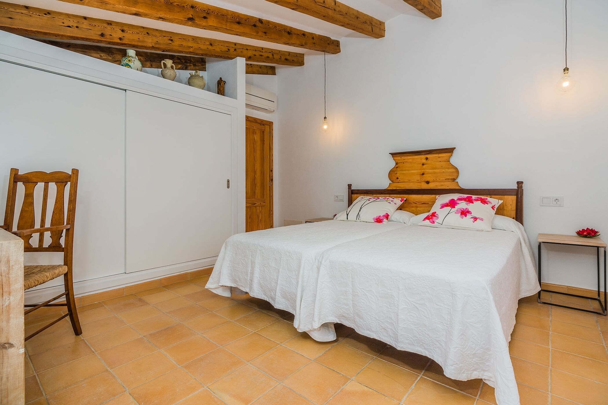 A bedroom with a wooden bed frame, white bedding, and a wooden chair.