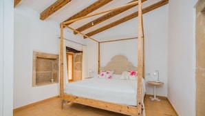 Een hemelbed met houten frame, een klein nachtkastje met lamp en een raam met gordijn.