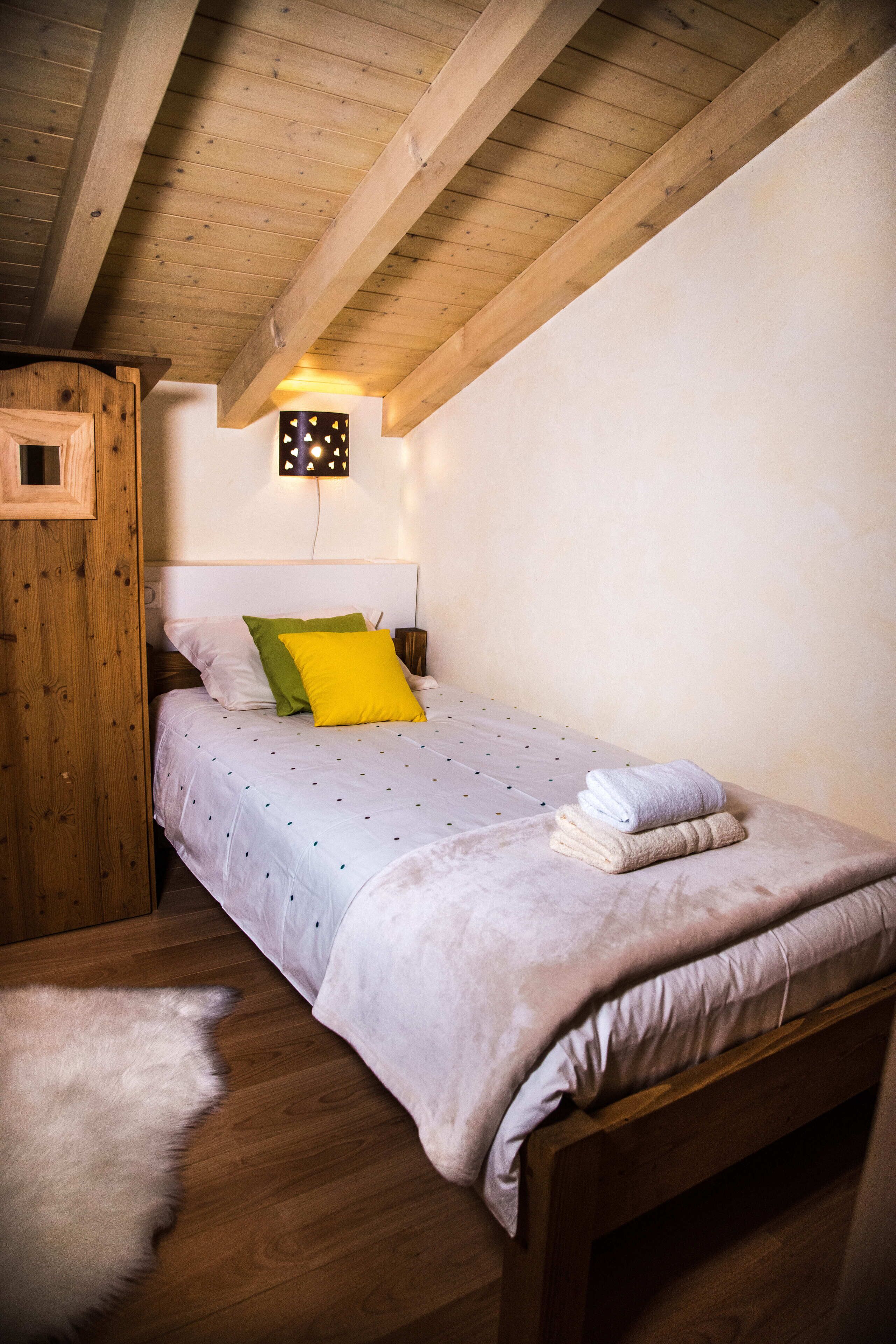 A single bed with a wooden headboard, a small nightstand, and a wall-mounted light fixture.