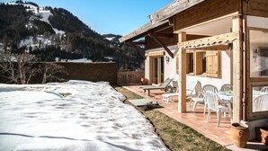 Un chalet con un patio, mobiliario exterior y vistas a montañas nevadas.