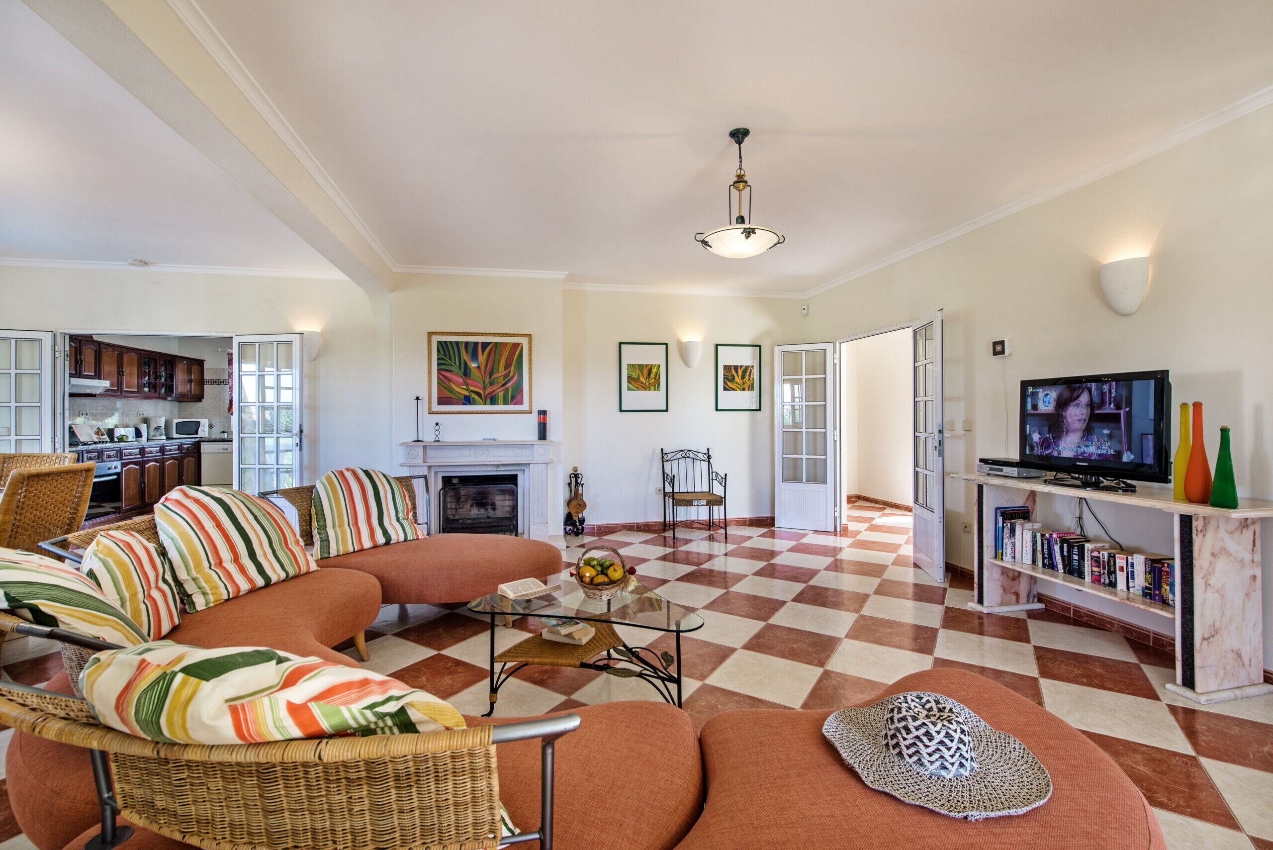 A living room with a checkered floor, a fireplace, a television, and a dining area with a kitchen in the background.