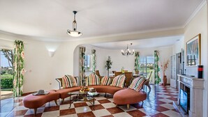 A spacious living room with a checkered floor, a curved sofa with striped cushions, a coffee table with fruit, and a fireplace.