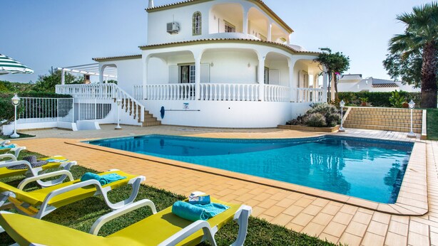 A white villa with a swimming pool, a covered patio, and a garden.