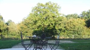 A metal outdoor table and chairs set on a paved area, surrounded by trees and greenery. - Country holiday home  independant and calm (Ouzouer-Sur-Trézée)