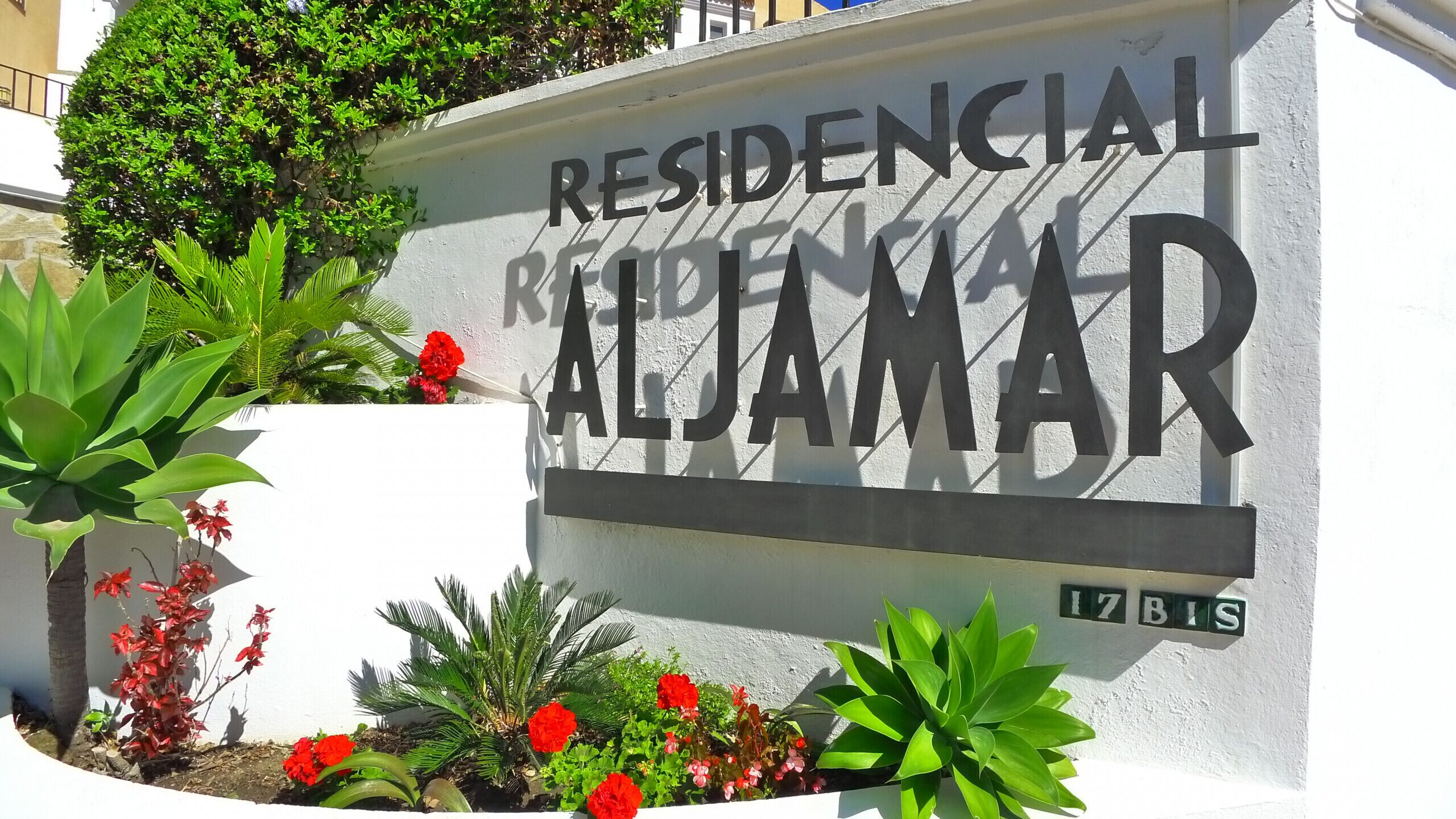 A sign for 'Residencial Aldamar' with a white wall and green plants.