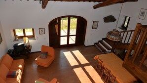 A spacious living room with a wooden ceiling, a large arched doorway, and a dining area with a table and chairs.