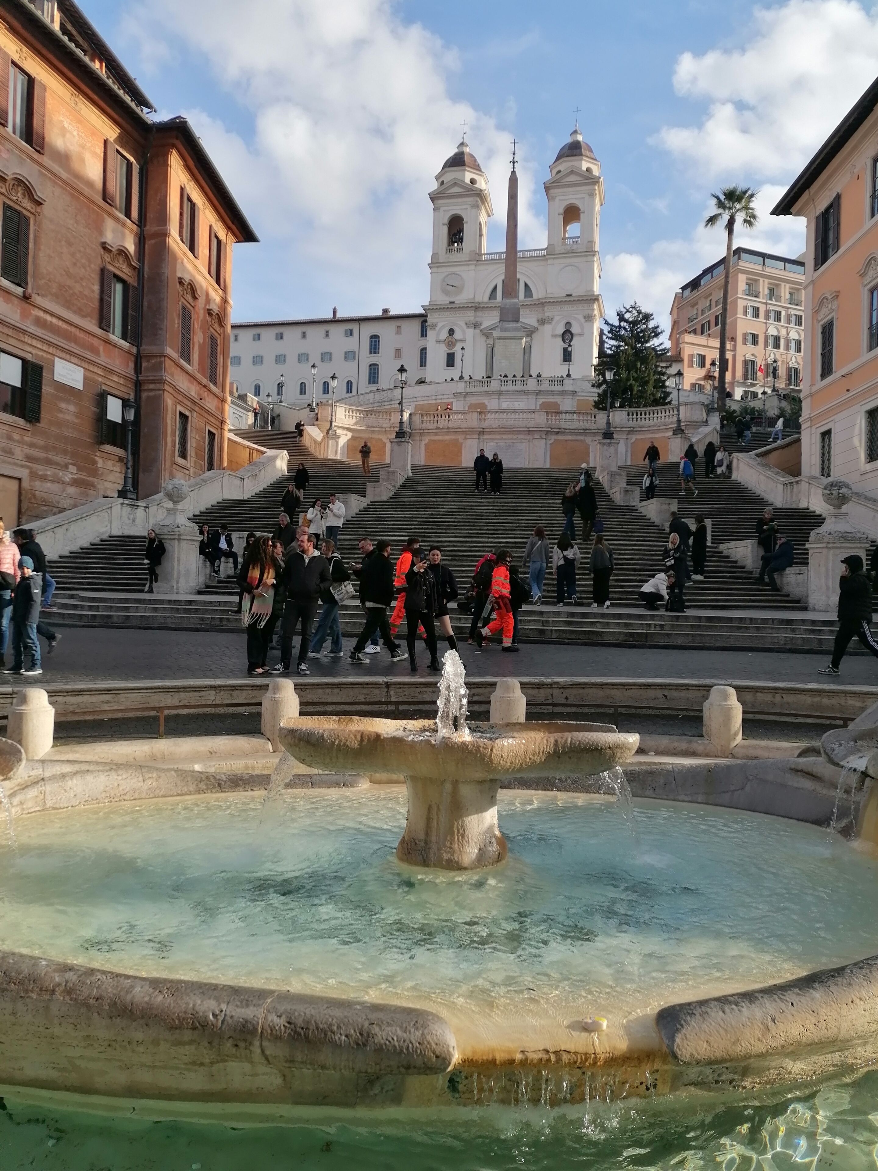 A historic square with a fountain, steps leading to a church, and surrounding buildings.