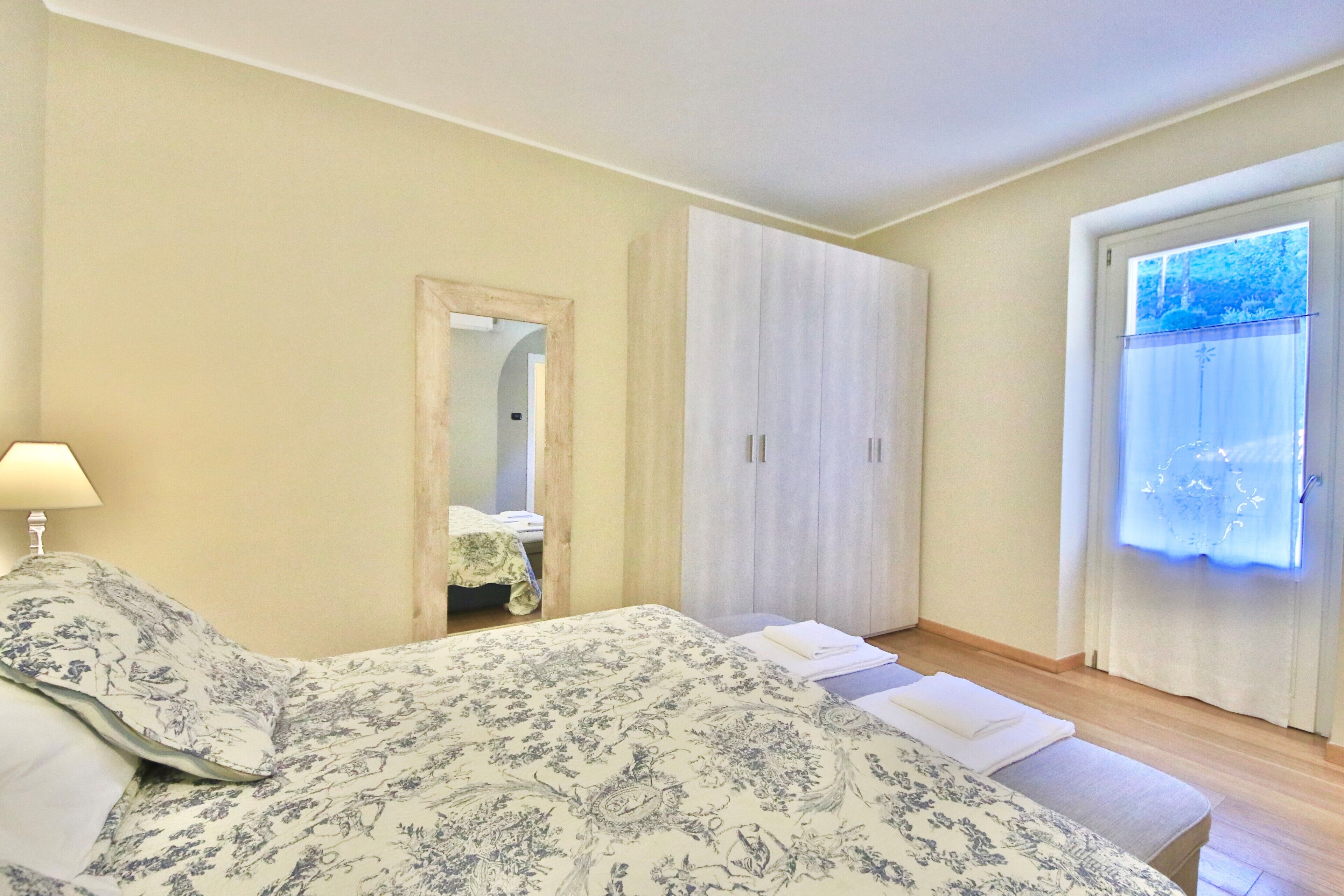 Een slaapkamer met een bed, een kledingkast, een spiegel en een raam met gordijnen.