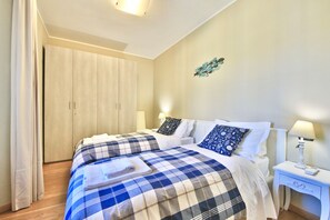 A bedroom with two beds, a wardrobe, bedside tables, and a wall decoration. - RENZO by KlabHouse-Central 2BDR lakeview w/AC (Bellagio)